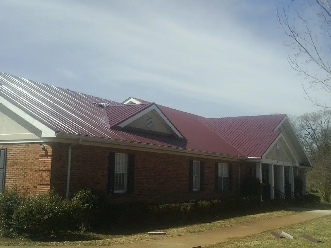 Red metal roof with gabled entries on a long brick building, from a Hail Damage Roof Repair job in Snow Camp