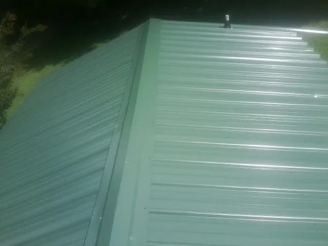 New green metal panels meeting at the ridge of a roof — Flat Roof Repair work by our crew in Snow Camp