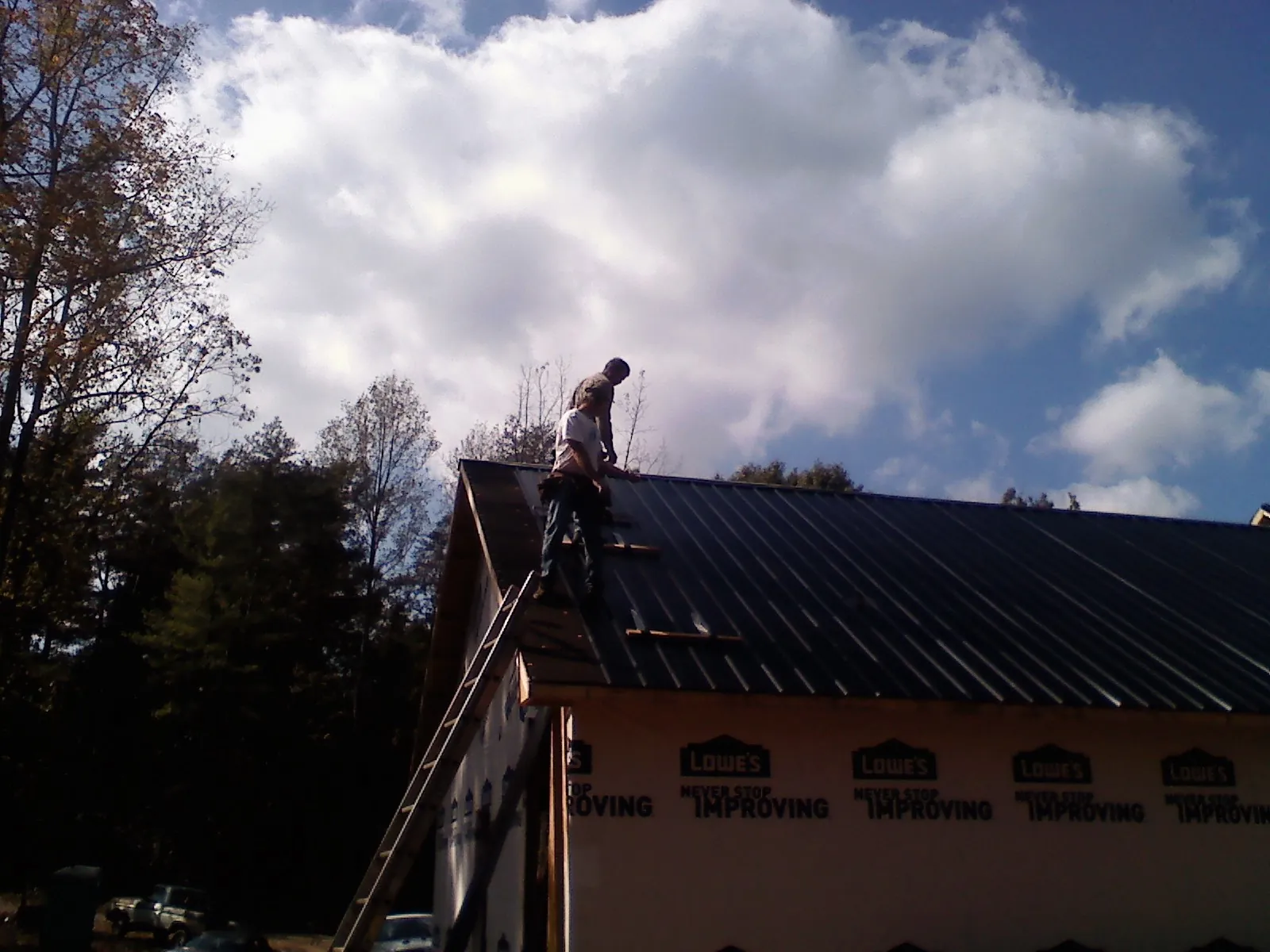 Roofer fastening dark metal panels high against a cloudy sky, from a Roof Inspection job in Snow Camp