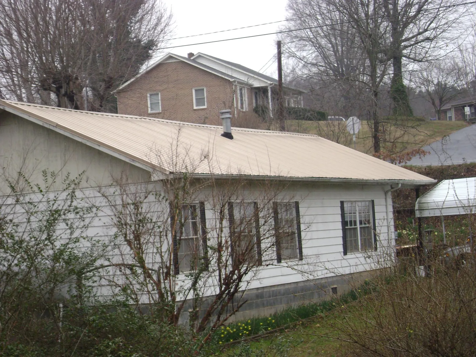 Tan metal roof on a white sided house set into a hillside — Commercial Roofing by Roofing Brothers in Snow Camp