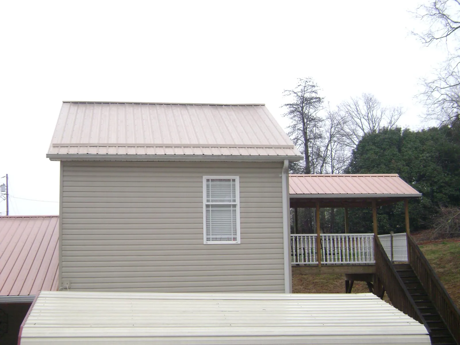 Tan metal roofs on a two story addition and attached porch, from a Roof Replacement job in Snow Camp